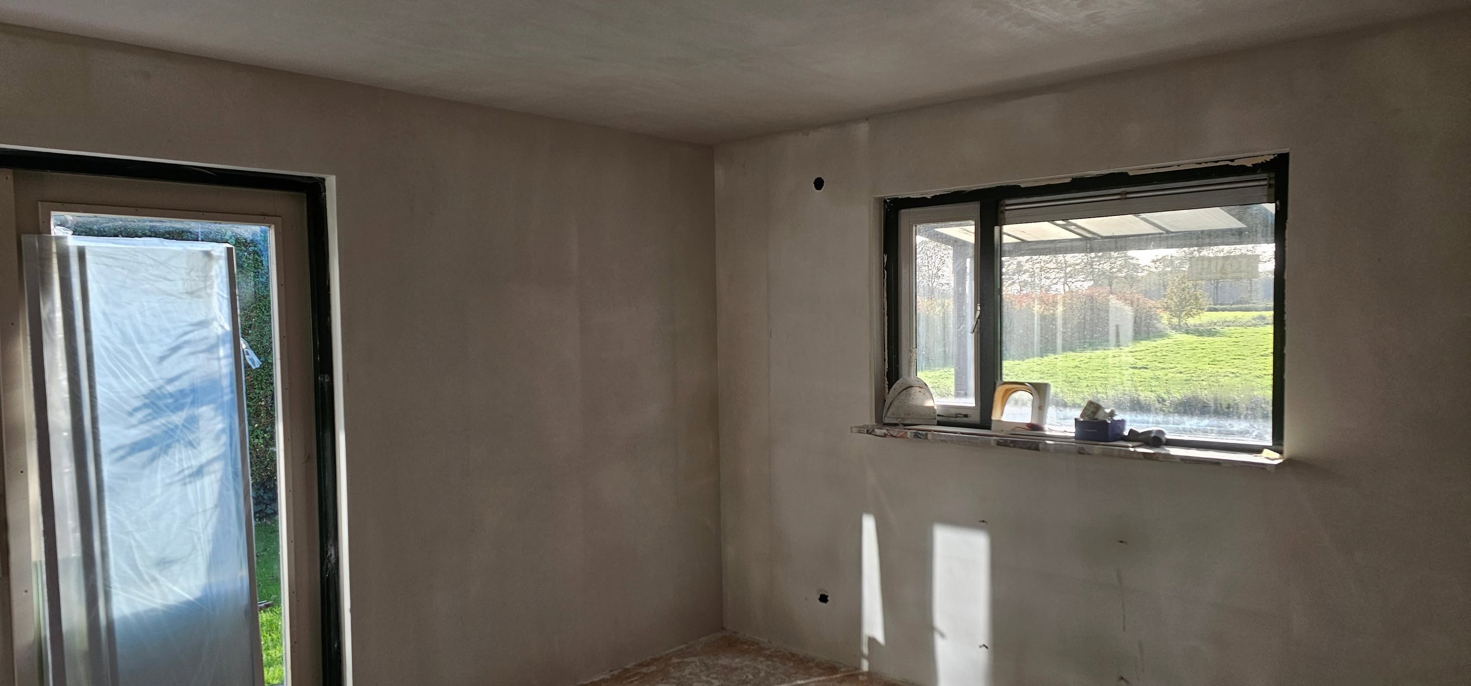 Lege kamer met vers gestucte wanden en plafond, zon valt door het raam naar de tuin
