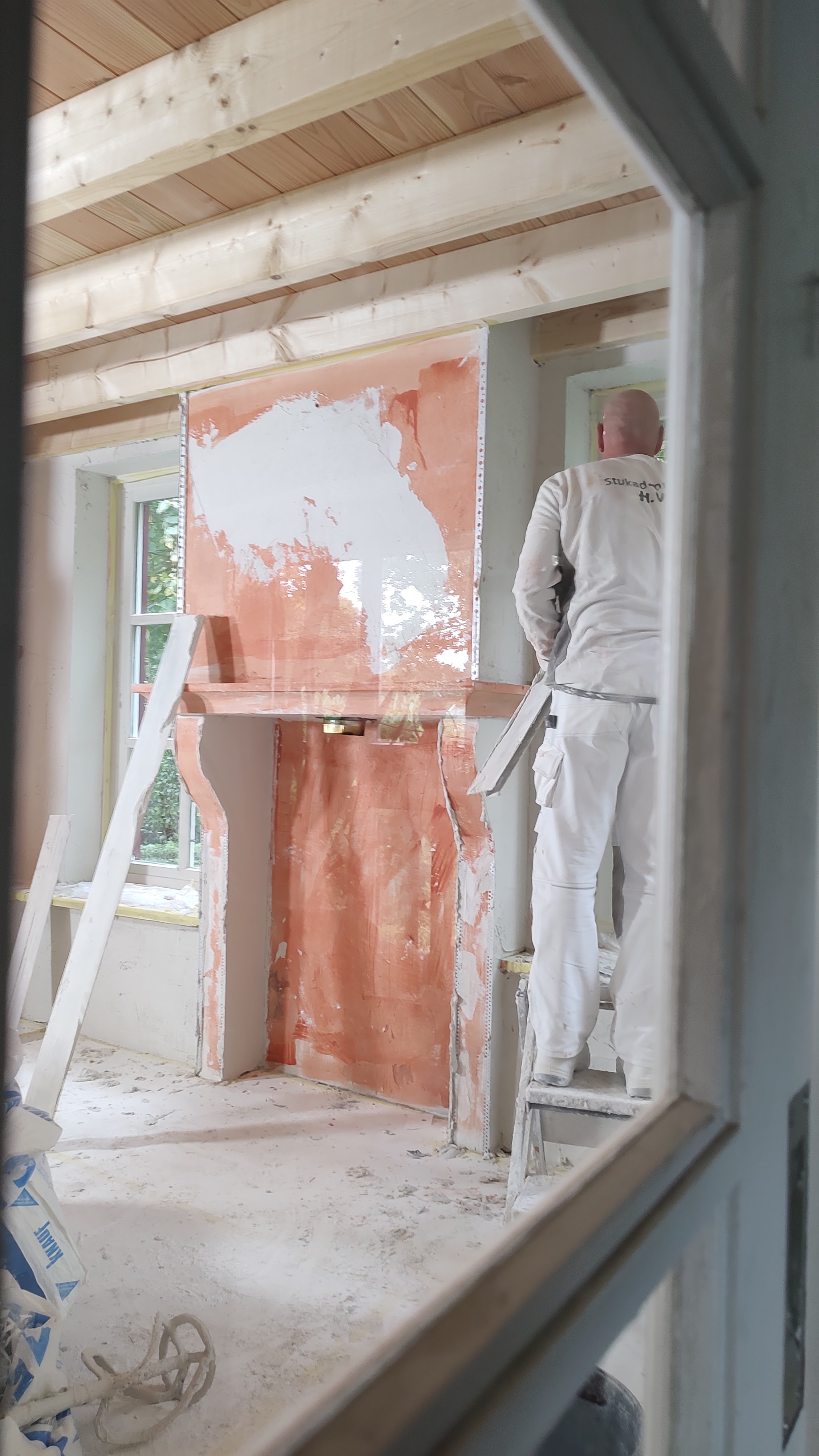 Henk in witte werkkleding op een trap, bezig met het stucwerk van een schoorsteenmantel
