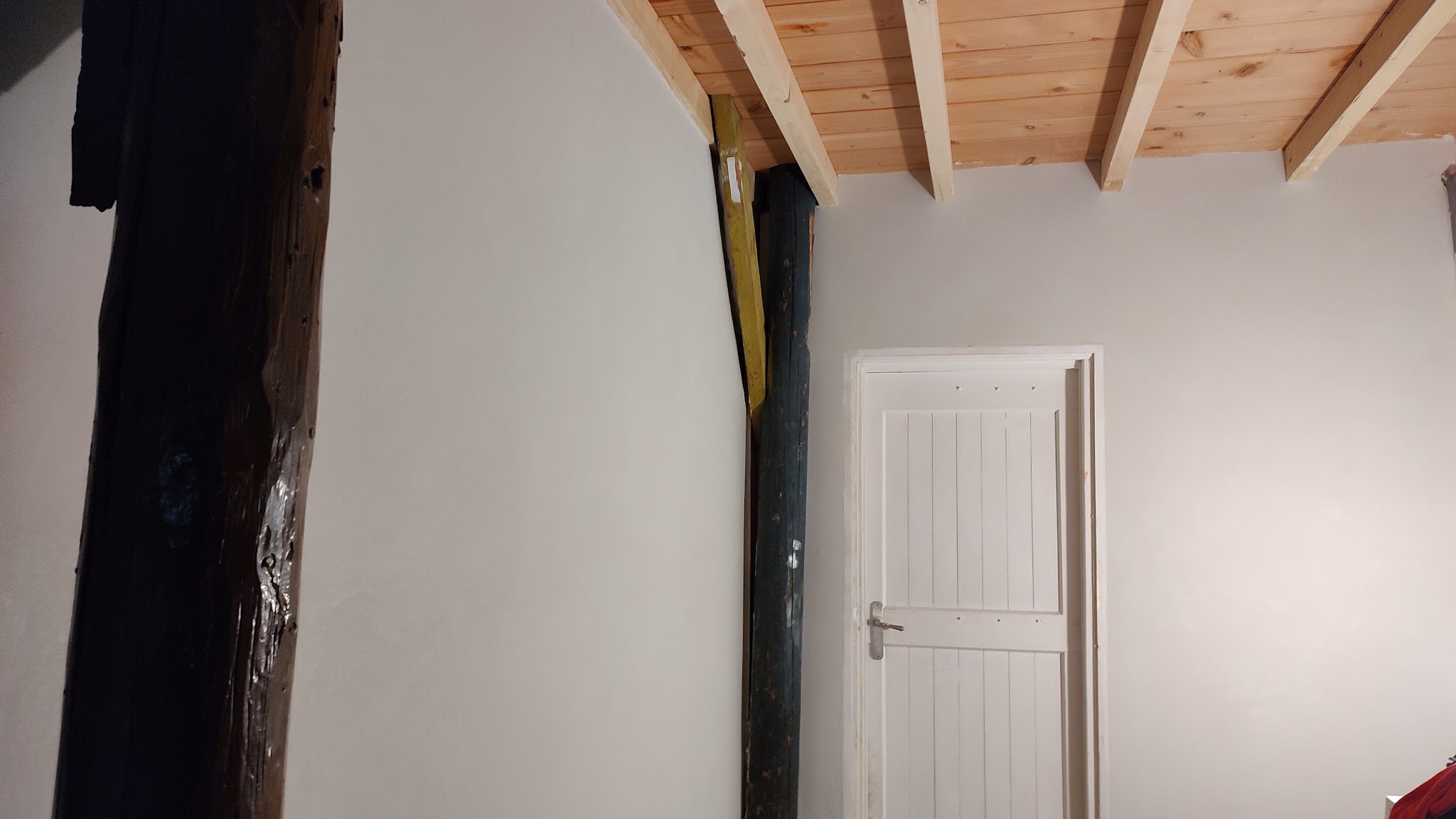 Glad gestucte witte wand tussen oude donkere balken, met een houten plafond